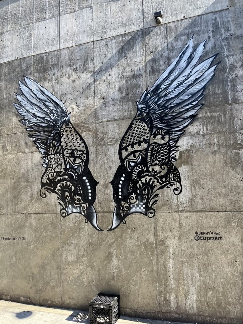 Exterior image of a gray building painted with an outline of wings in black