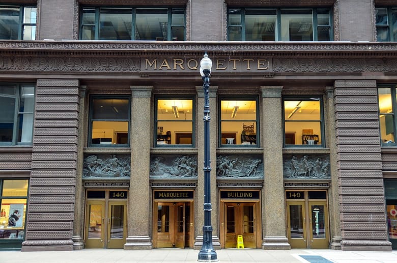 Exterior shot of a building with sculptures carved in relief above the door and dark walls.