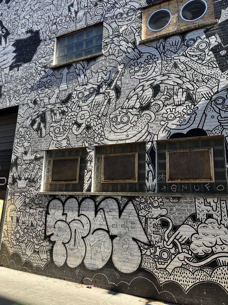 Exterior image of a brick building painted with a black and white mural of line art illustrating characters and shapes
